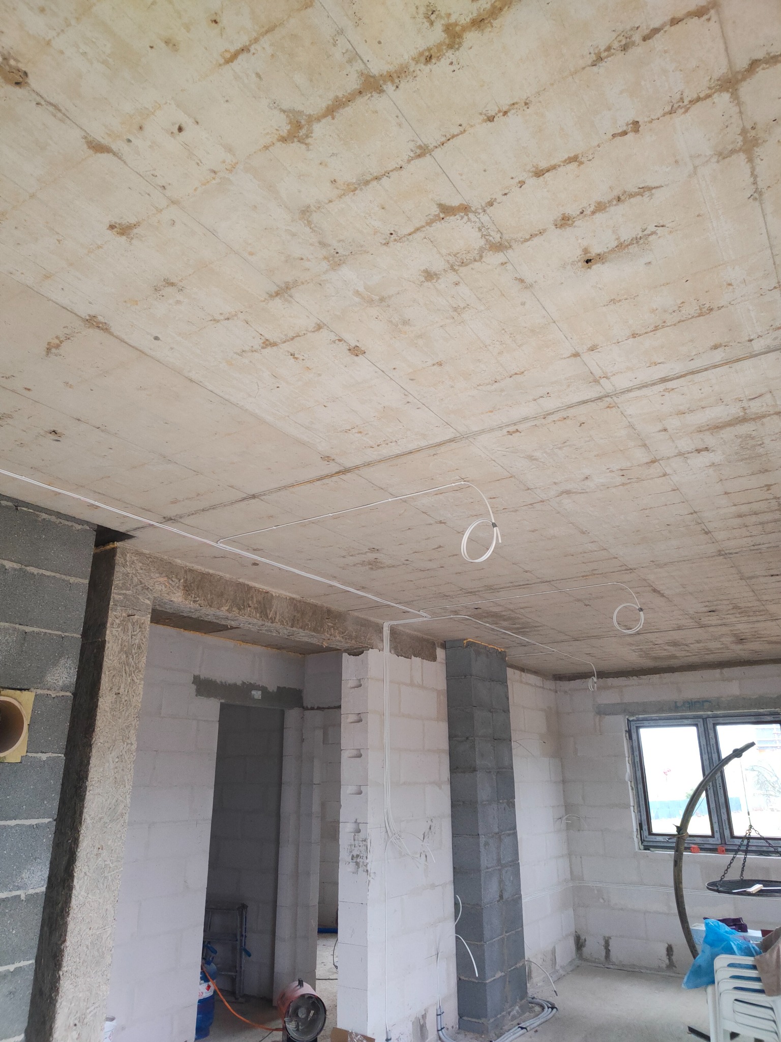 Surowy betonowy strop z widocznymi śladami szalunku i prowadzonymi przewodami elektrycznymi, ściany z bloczków betonowych i gazobetonowych w surowym stanie, widoczne przygotowania do dalszych prac...