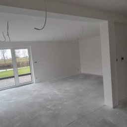 Best House - Surowe wnętrze po nałożeniu gładzi w Janowie Lubelskim, widoczne wystające przewody instalacji elektrycznej i widok z okna na zewnątrz.