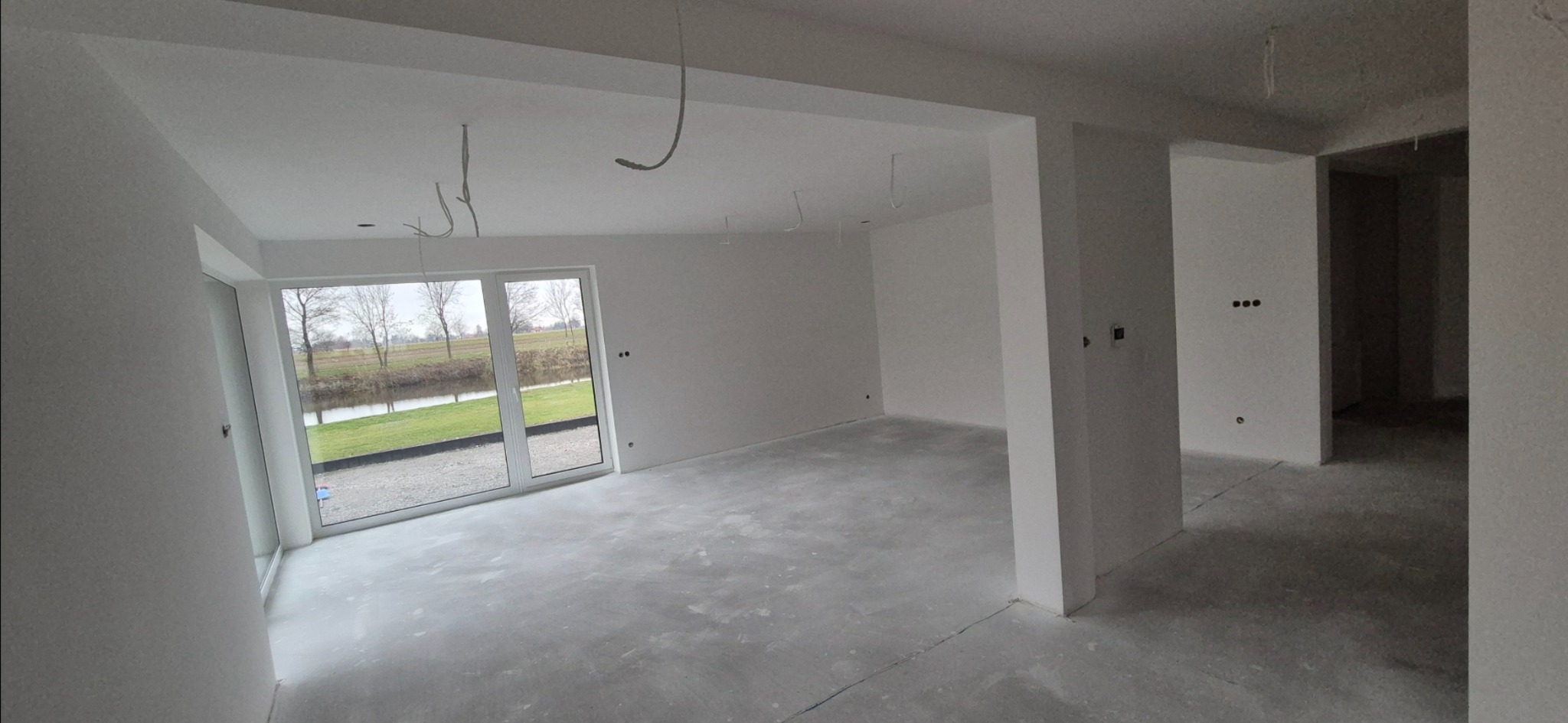 Surowe wnętrze po nałożeniu gładzi w Janowie Lubelskim, widoczne wystające przewody instalacji elektrycznej i widok z okna na zewnątrz.