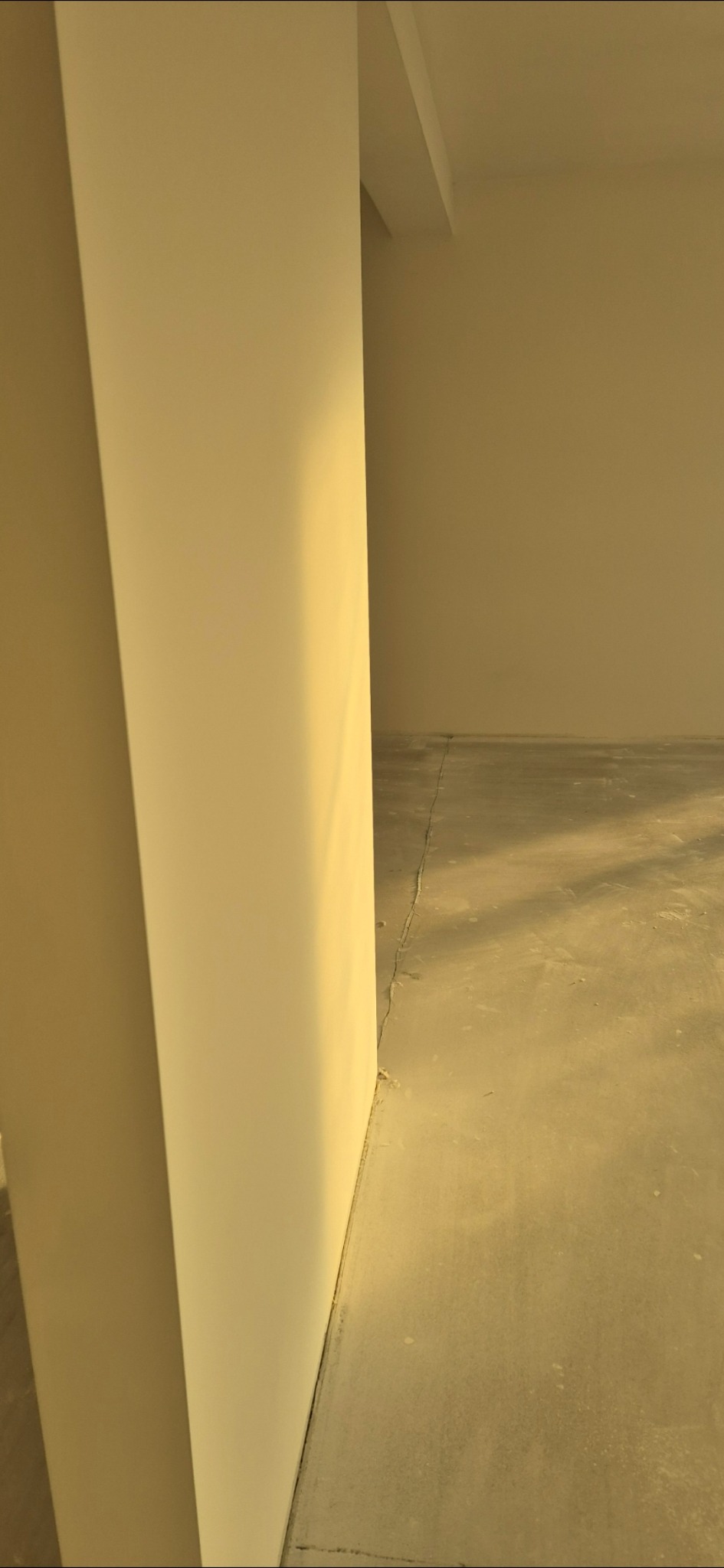 Pusta przestrzeń w trakcie prac remontowych, widoczny fragment kolumny i surowy beton na podłodze, oświetlony ciepłym światłem.
