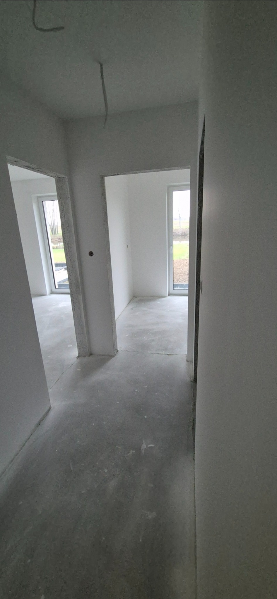 Surowe wnętrze w trakcie prac wykończeniowych: szare wylewki, białe ściany przed malowaniem, widoczne kable ze stropu.