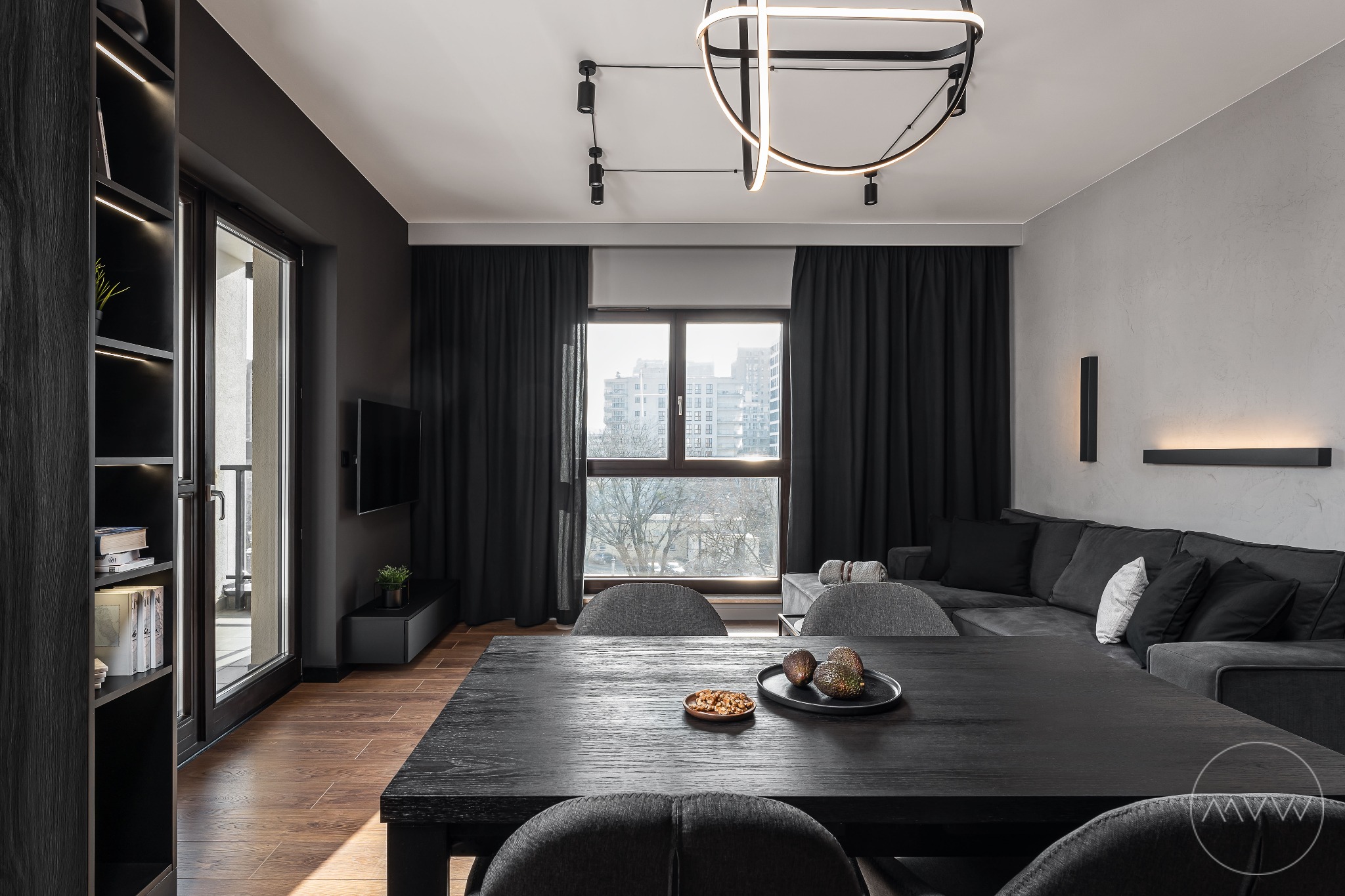 Nowoczesna aranżacja salonu z jadalnią w Gdańsku. Ciemne meble, drewniana podłoga, minimalistyczne oświetlenie i widok na miasto przez okno.