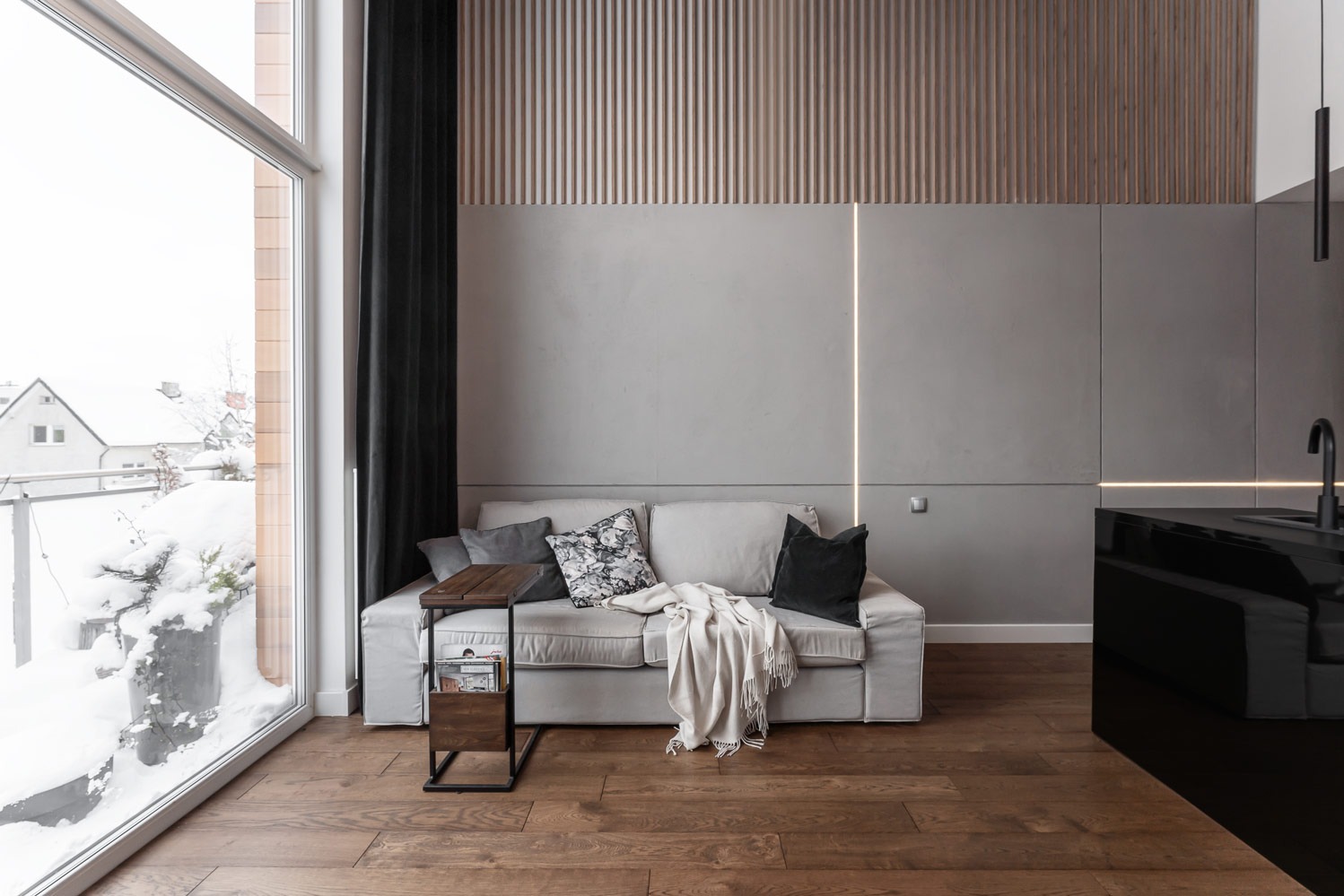 Jasny salon z sofą, drewnianą podłogą i dużym oknem z widokiem na zaśnieżony krajobraz, oświetlenie LED w ścianie.
