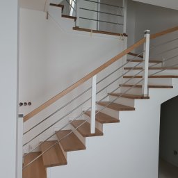 PHU DĄB-DEKOR KATARZYNA JEWULSKA - Nowoczesne schody drewniane z białymi stopnicami i metalową balustradą, oświetlone naturalnym światłem, widoczne gniazdka elektryczne na ścianie.