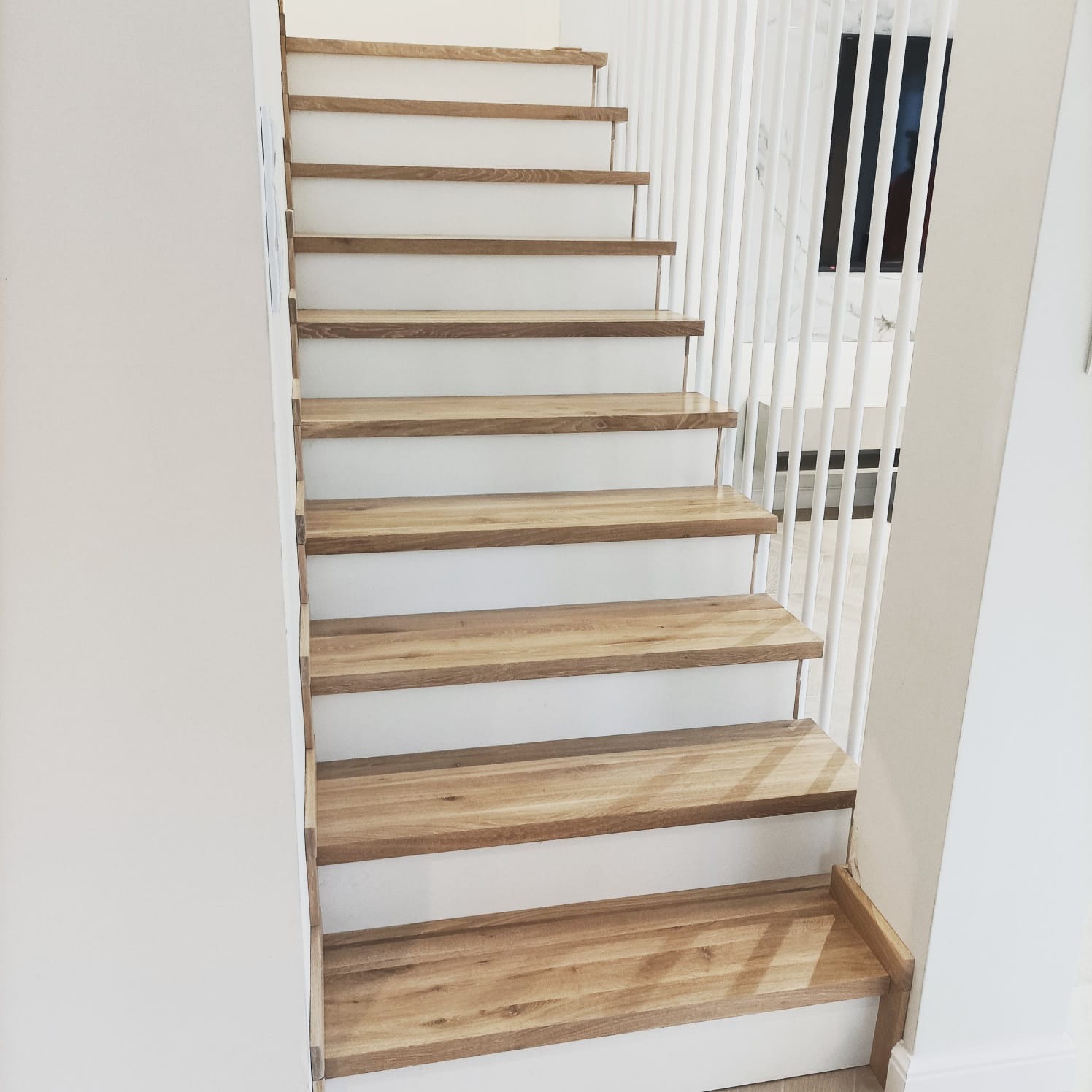 Nowoczesne schody drewniane z białymi podstopnicami i ażurową balustradą, widok z dołu, jasne wnętrze. Stopnie z naturalnego drewna.