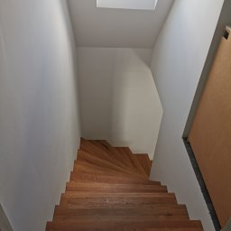 Kw-Kris Bud - Drewniane schody kręcone z jasnego drewna, widok z góry, białe ściany i okno dachowe w tle.