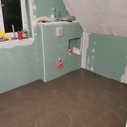 Kw-Kris Bud - Wnętrze łazienki w trakcie prac: wylewka podłogowa, ściany obłożone płytami kartonowo-gipsowymi, widoczne instalacje hydrauliczne, narzędzia i materiały budowlane na parapecie okiennym.