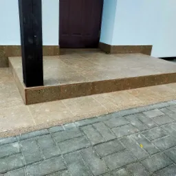 Wyłożone płytkami schody wejściowe do domu z ciemnymi drewnianymi słupami, widok z góry na kostkę brukową.