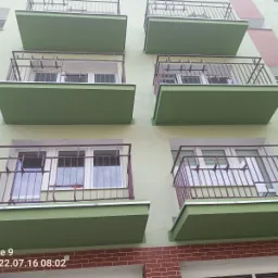 Fasada budynku wielorodzinnego z balkonami w kolorze zielonym i balustradami w kolorze bordowym, widok z dołu.