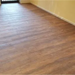 Ukończona podłoga z paneli imitujących drewno, widok z niskiej perspektywy, fragment ściany w kolorze żółtym i biała listwa przypodłogowa.