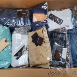 Kartonowe pudło wypełnione różnorodną odzieżą markową, każda sztuka zapakowana w przezroczysty plastik, widoczne dżinsy Pepe Jeans, Wrangler, Levi's, koszula Scotch & Soda, spodnie Gant i inne,...