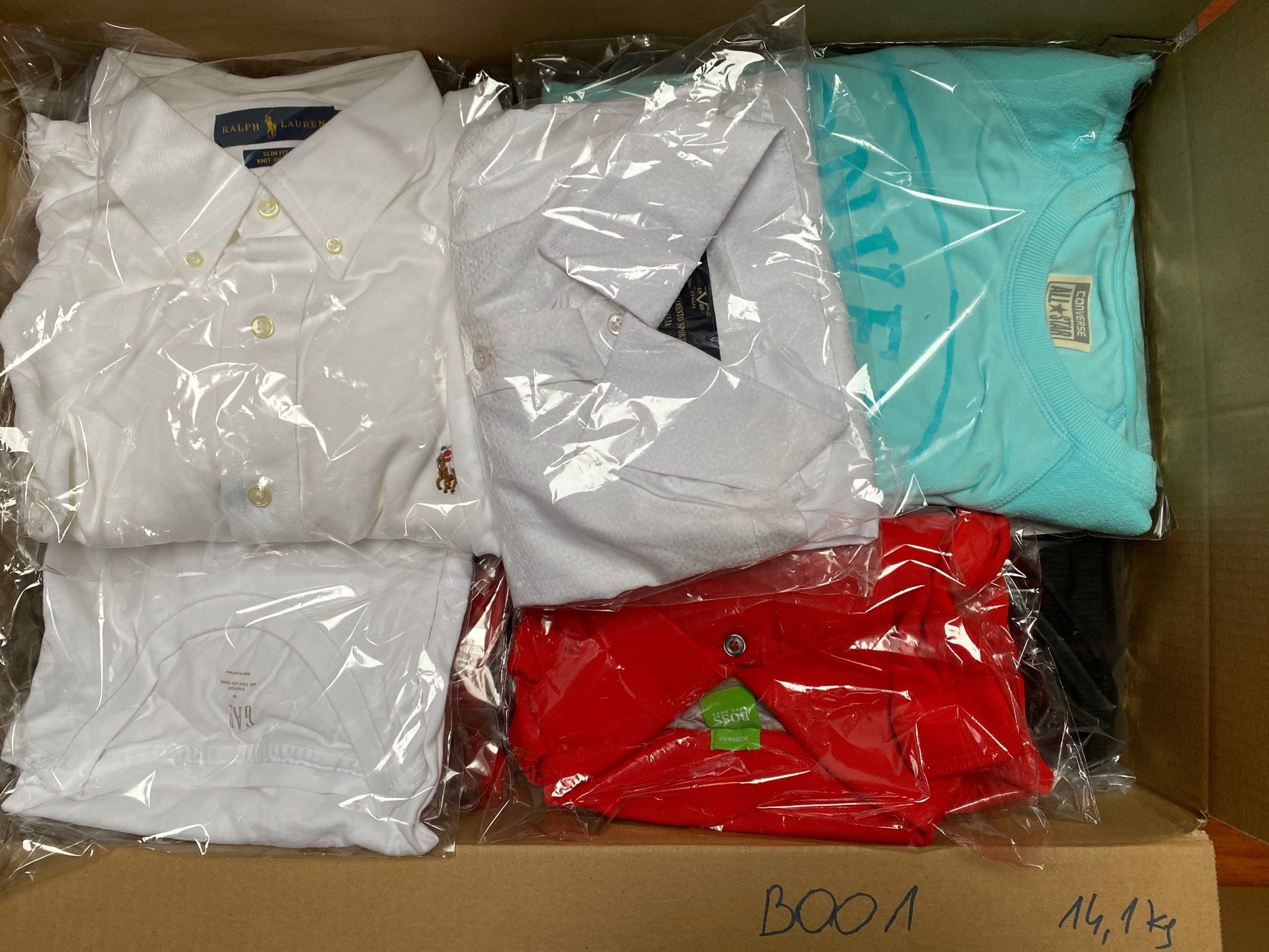 Kartonowe pudełko wypełnione różnorodną odzieżą, w tym koszule z kołnierzykiem Ralph Lauren, t-shirty Converse All Star i Boss, zapakowane w plastikowe torby, widoczne napisy 'BOO1' i '14,1kg'...
