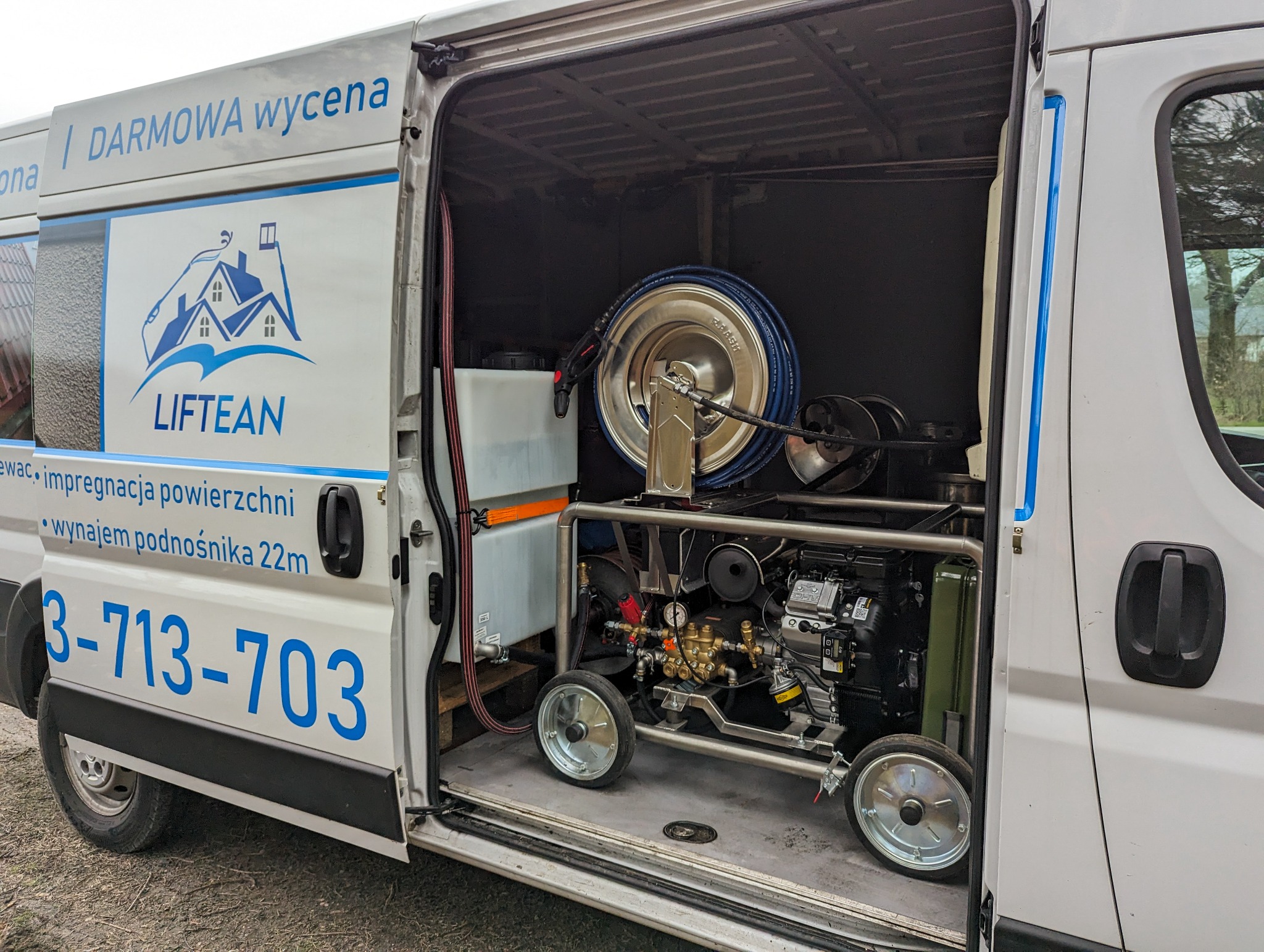Wnętrze białego furgonu z otwartymi drzwiami bocznymi, ukazujące mobilną myjkę ciśnieniową z bębnem na wąż i zbiornikiem na wodę. Na karoserii furgonu widoczne logo firmy 'LIFTEAN' i numer telefonu.