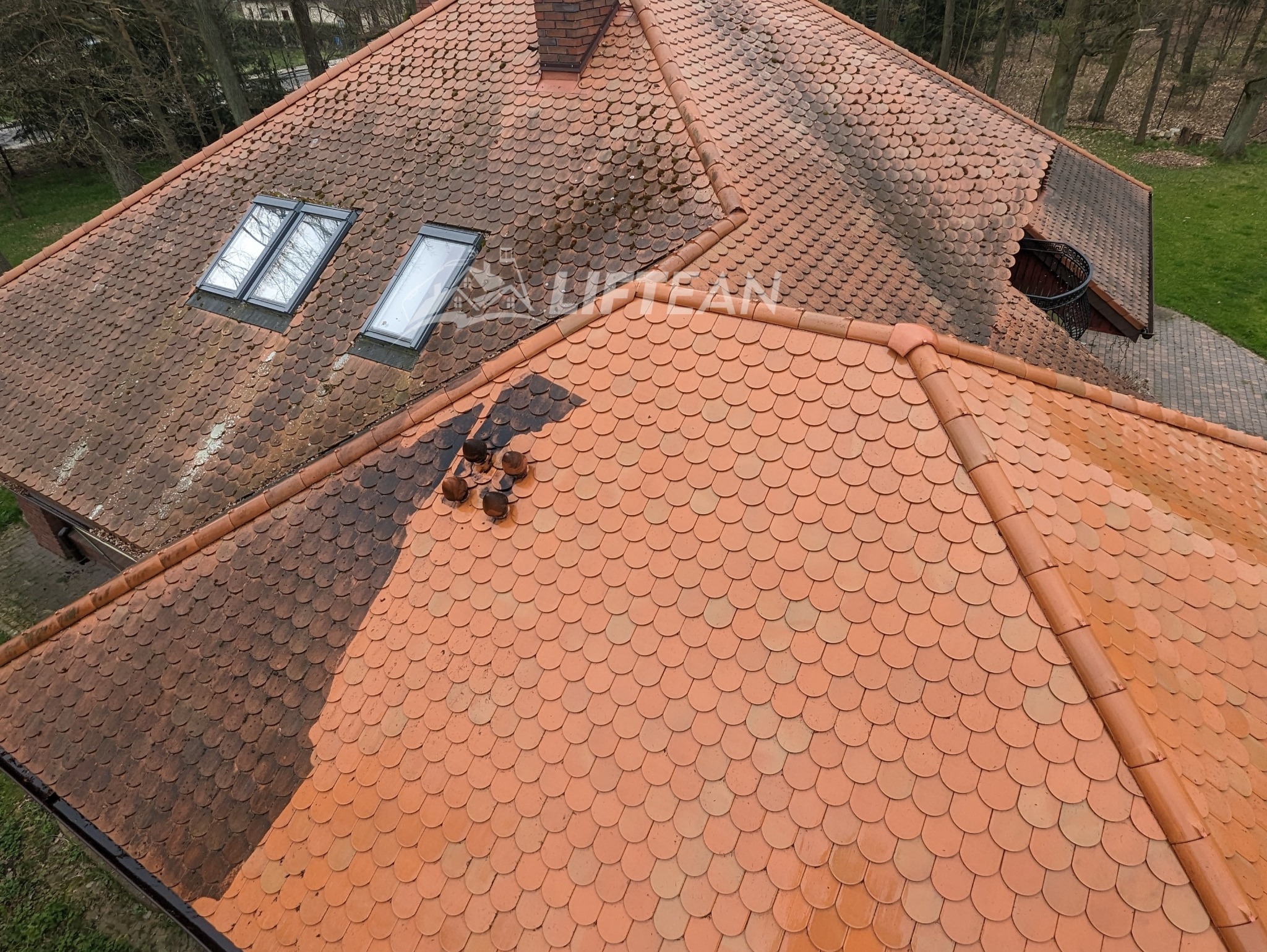 Częściowo oczyszczony dach z dachówki ceramicznej w odcieniach czerwieni, z widocznymi oknami dachowymi i kominem, ukazujący kontrast między umytą a zabrudzoną powierzchnią.