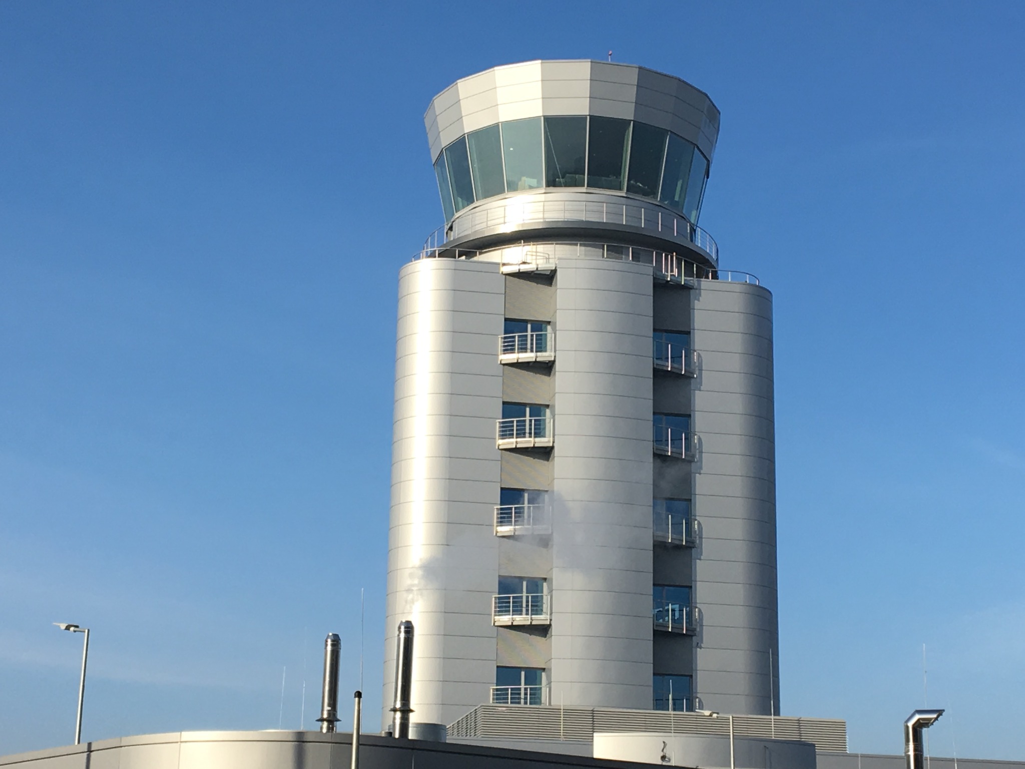 Nowoczesna wieża kontroli lotów z panoramicznymi oknami i balkonami, widoczna instalacja odgromowa oraz kominy wentylacyjne na dachu