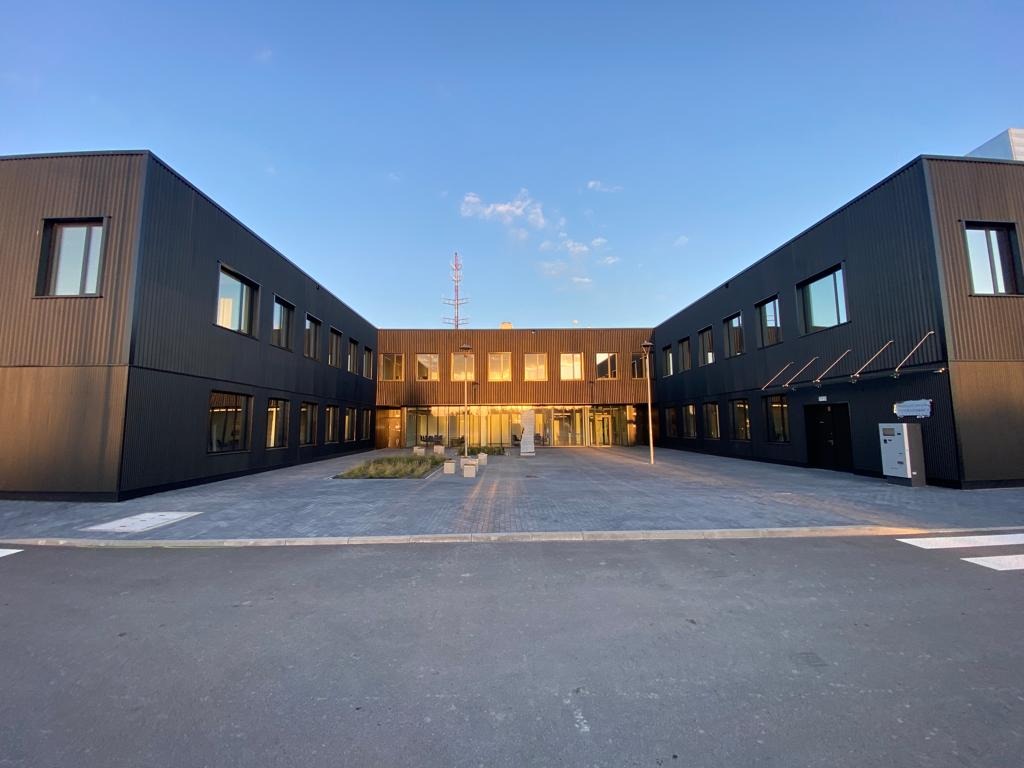 Nowoczesny budynek biurowy z ciemną elewacją i licznymi oknami, oświetlony popołudniowym słońcem, widoczna instalacja odgromowa na dachu.