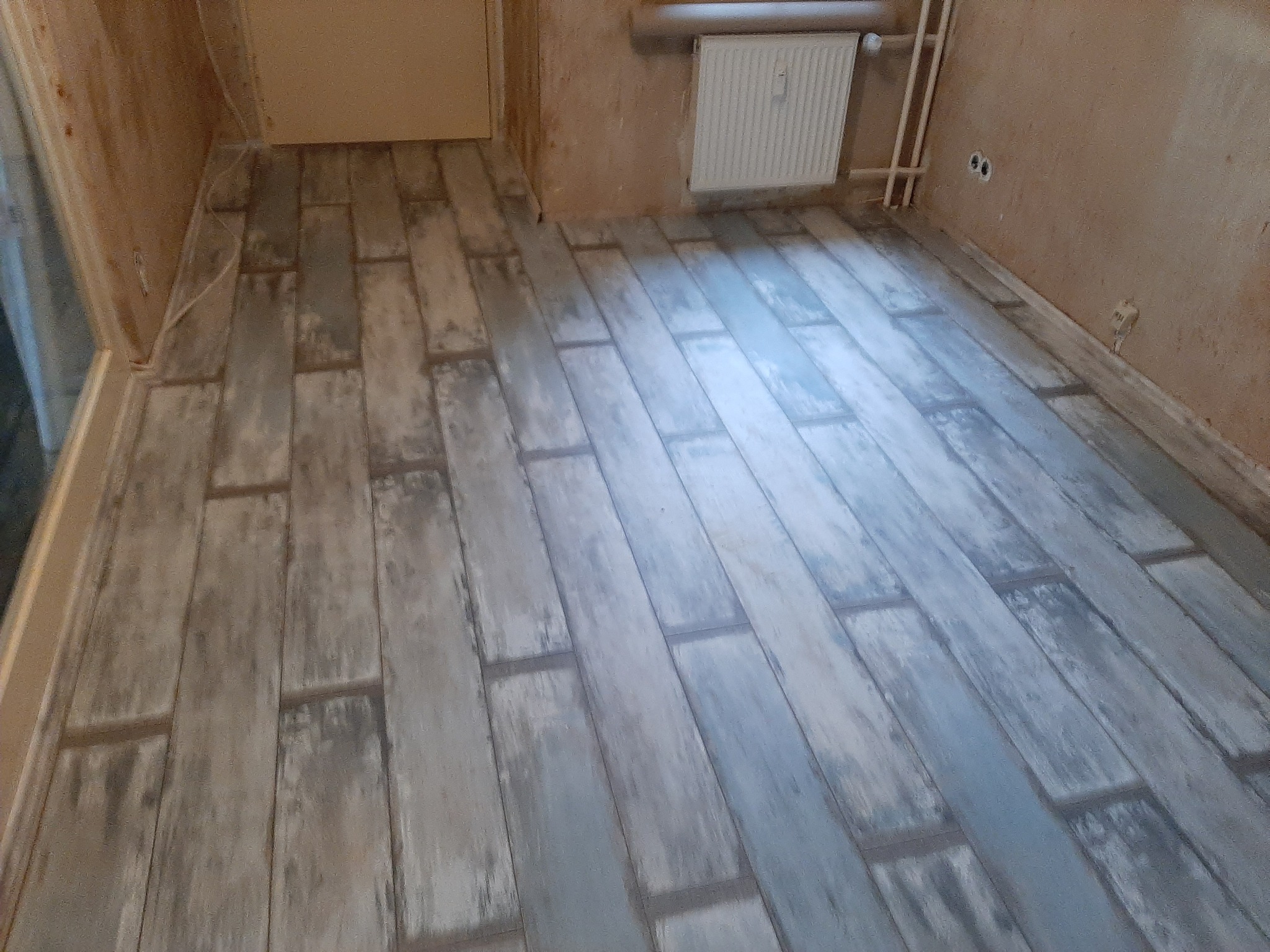 Ułożona podłoga z paneli imitujących postarzane drewno w pokoju przed odświeżeniem ścian, widoczny grzejnik i gniazdka elektryczne.