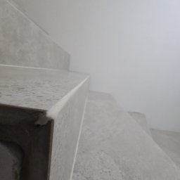 BUILD-MAX - Nowoczesne, szare schody z wykończonymi krawędziami, widziane z dołu pod kątem. Minimalistyczny design, jasne tło ściany, wysoka jakość wykończenia.