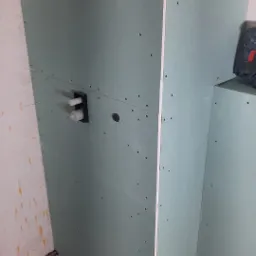 Płyta karton-gips na ścianie łazienki w trakcie montażu, widoczne przyłącza wodne i otwór pod instalację. W tle narzędzie. Prace wykończeniowe w surowym wnętrzu.