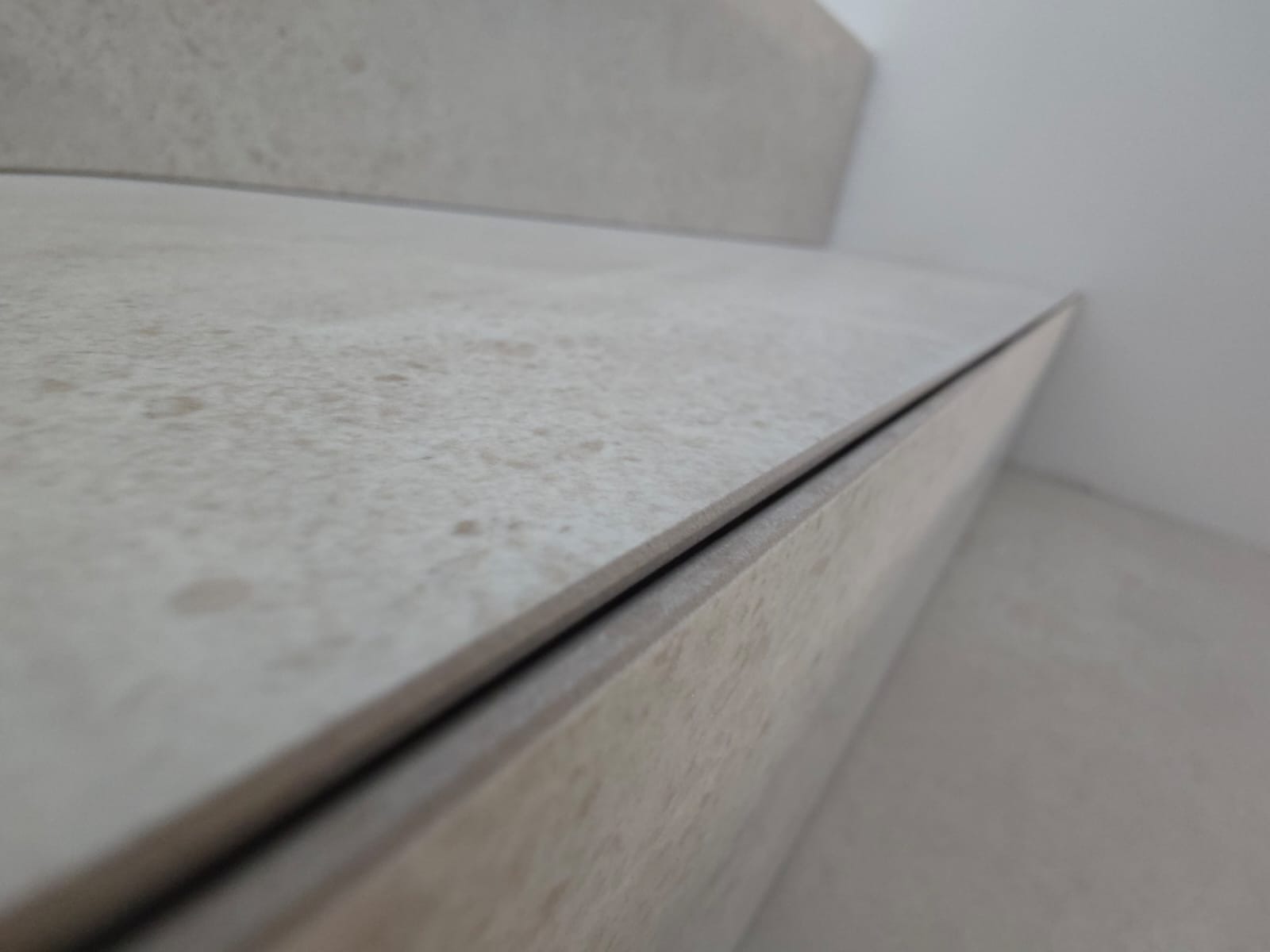 Beżowe płytki imitujące kamień, ułożone na schodach wewnętrznych. Widok z bliska na krawędź stopnia i podstopnicy, z delikatną fugą. Minimalistyczny design.