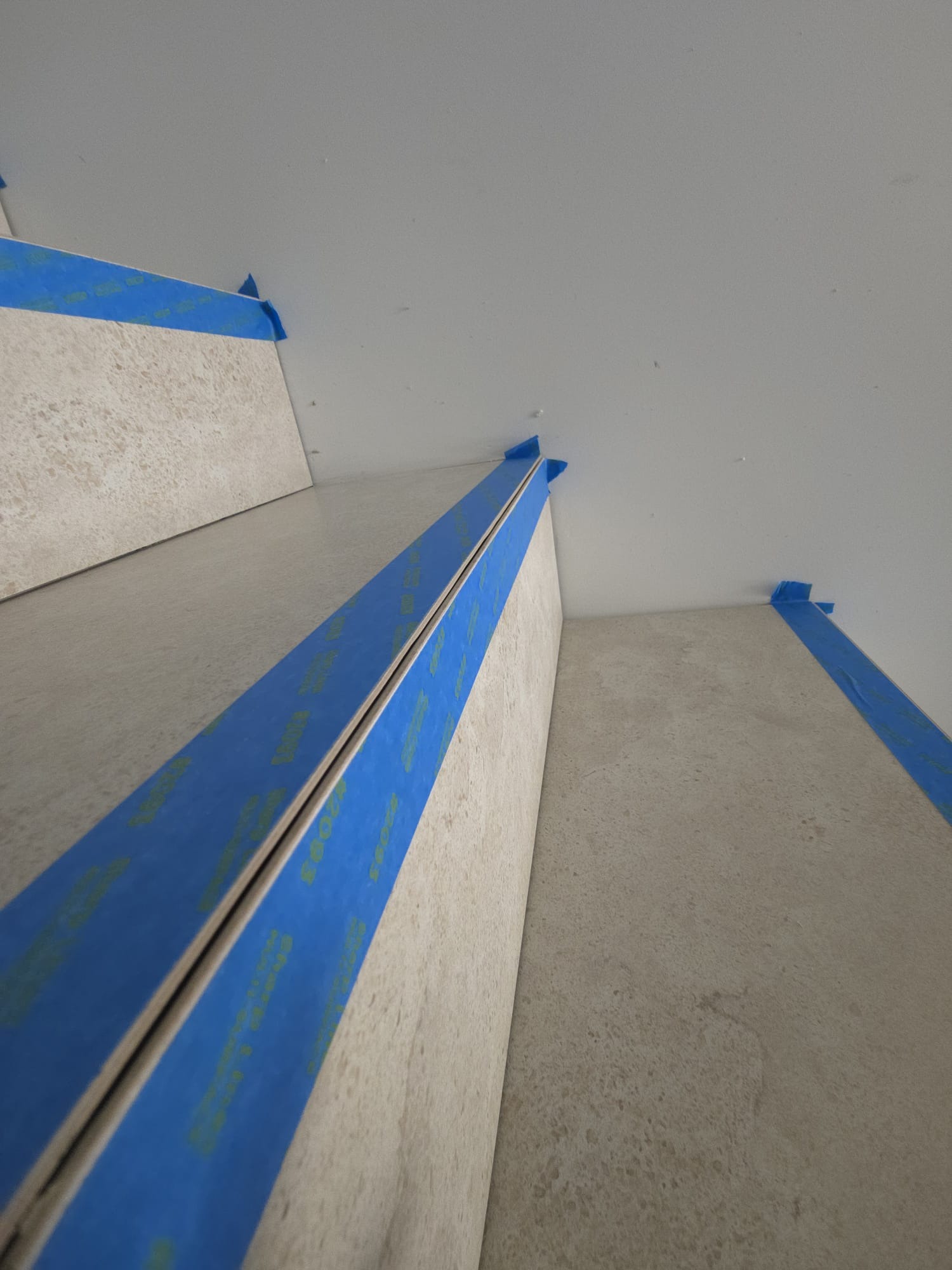 Ułożone płytki na schodach zabezpieczone niebieską taśmą malarską. Widok z dołu, bliska perspektywa.