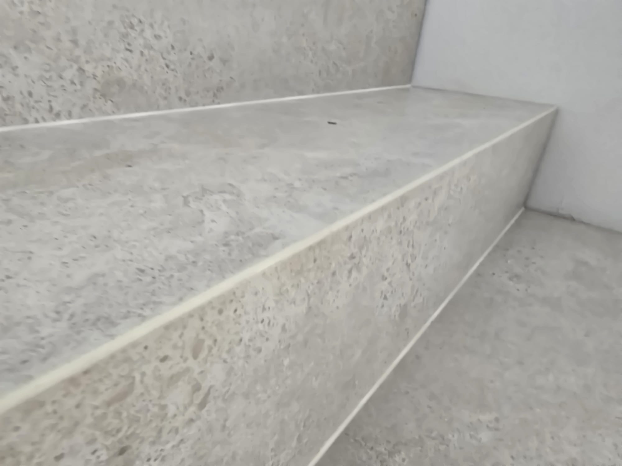 Wykończone schody z szarych, wzorzystych płytek ceramicznych, widoczne z bliskiej perspektywy. Minimalistyczny styl, jasne wnętrze, precyzyjne ułożenie płytek.