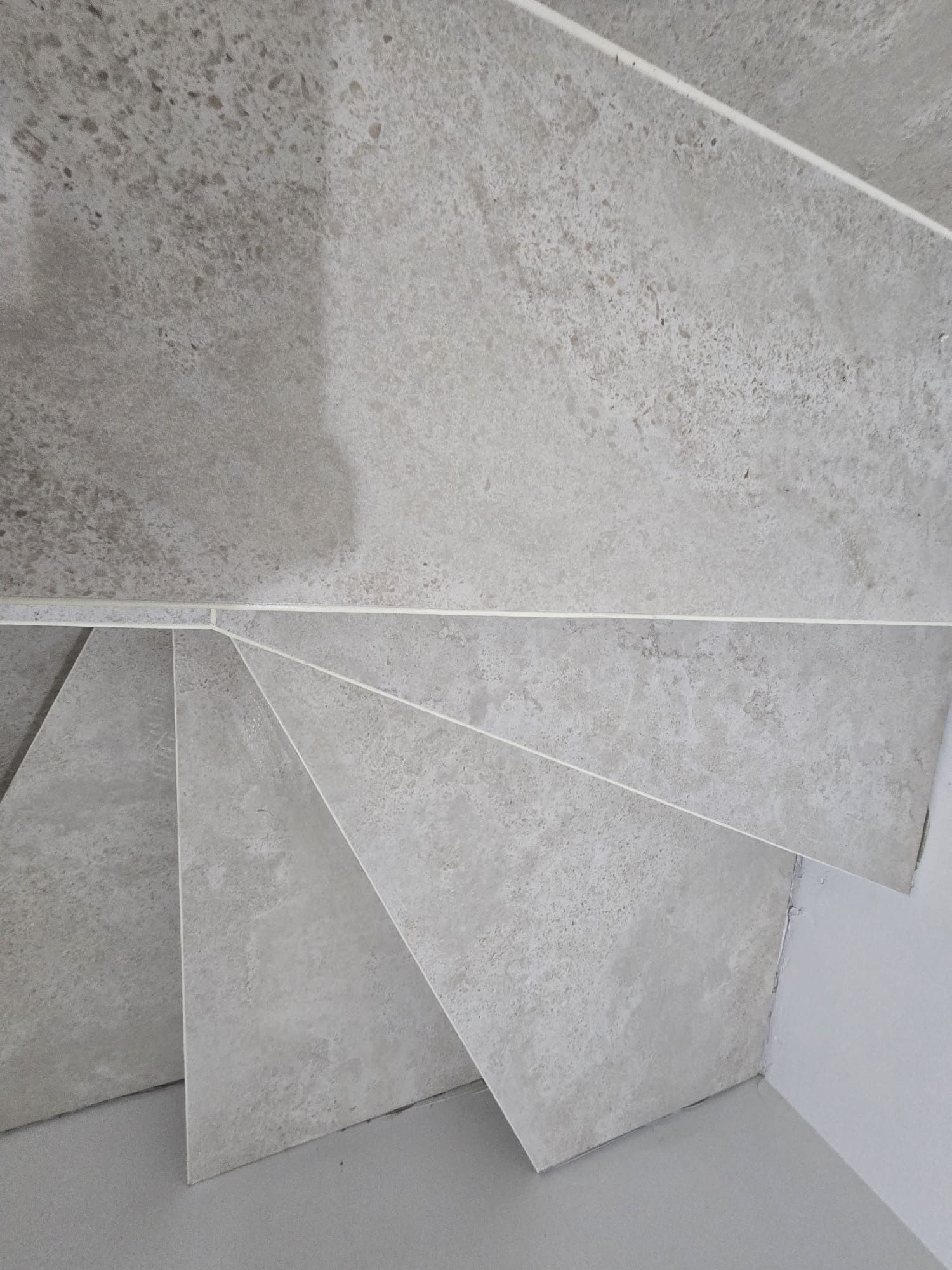 Wykończone schody z szarych, matowych płytek imitujących kamień, widok z góry, z precyzyjnie dociętymi krawędziami i fugami, minimalizm, nowoczesność.