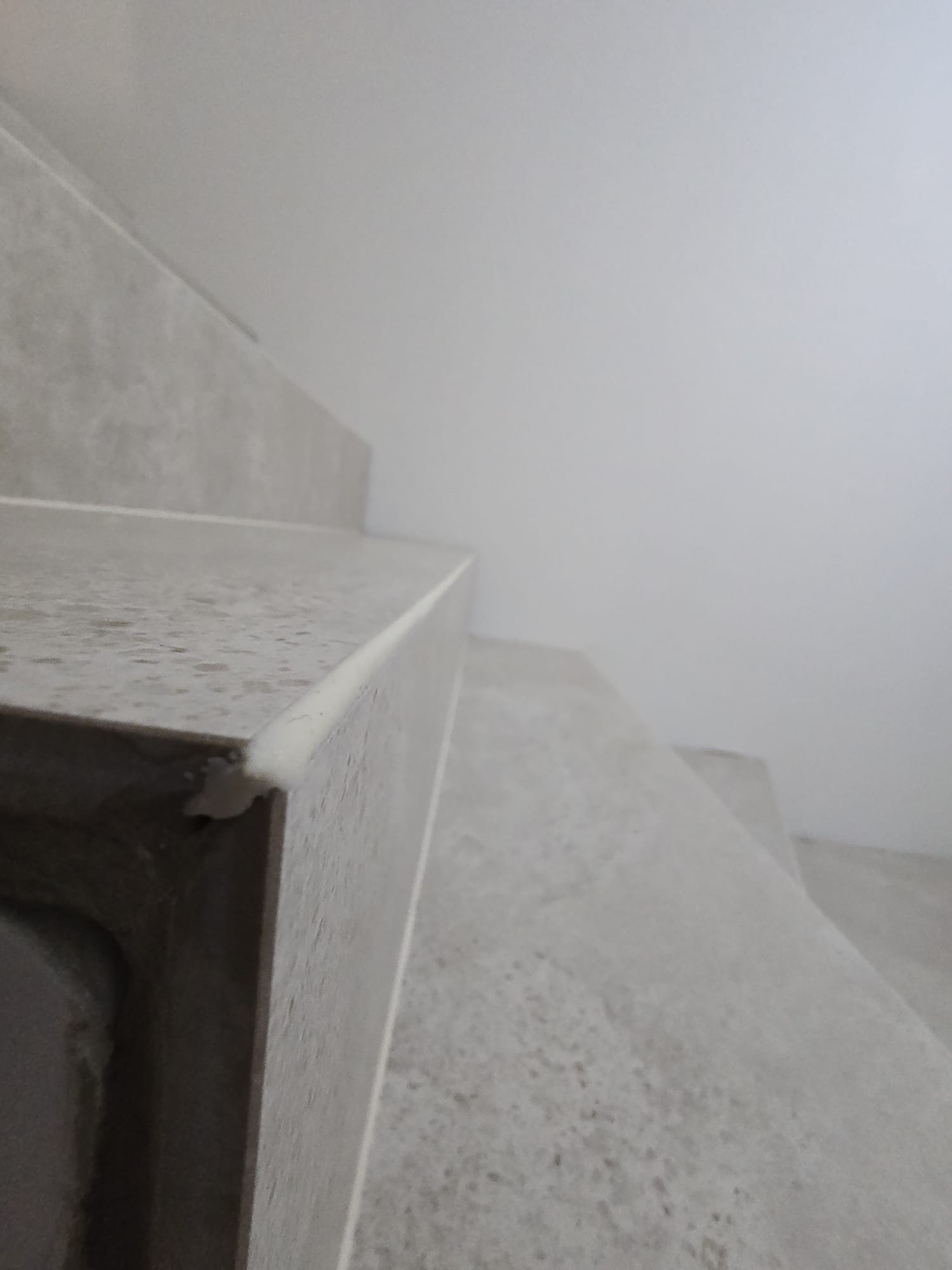 Nowoczesne, szare schody z wykończonymi krawędziami, widziane z dołu pod kątem. Minimalistyczny design, jasne tło ściany, wysoka jakość wykończenia.