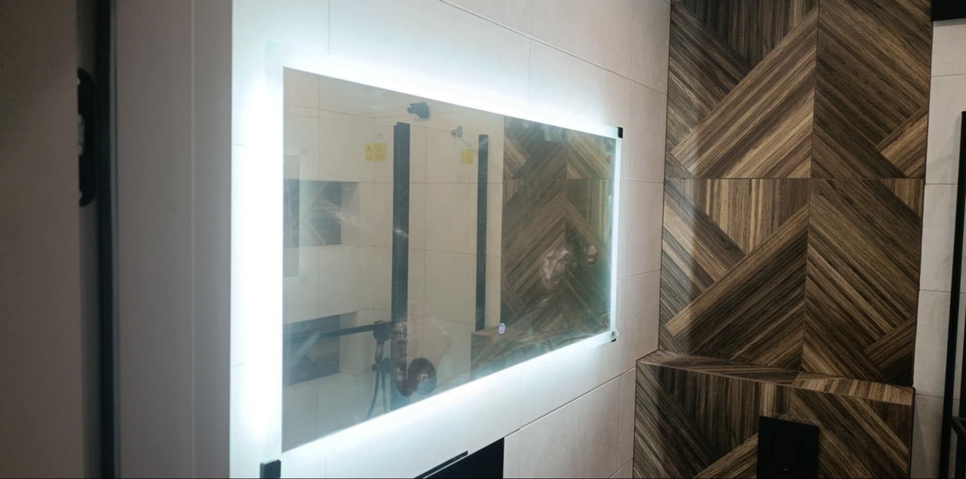 Nowoczesna łazienka z podświetlanym lustrem i dekoracyjną ścianą z płytek imitujących drewno ułożonych w geometryczny wzór.