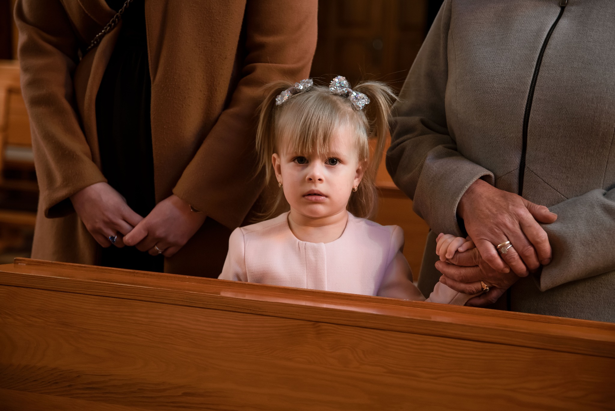 Dziewczynka z ozdobami we włosach w kościele, trzymająca dłoń starszej kobiety, reportaż.