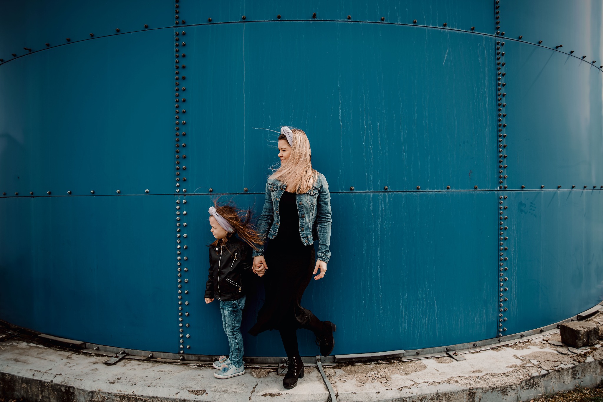 Matka z córką w Łodzi pozują na tle dużej, błękitnej konstrukcji, obie ubrane w kurtki, włosy rozwiane wiatrem.