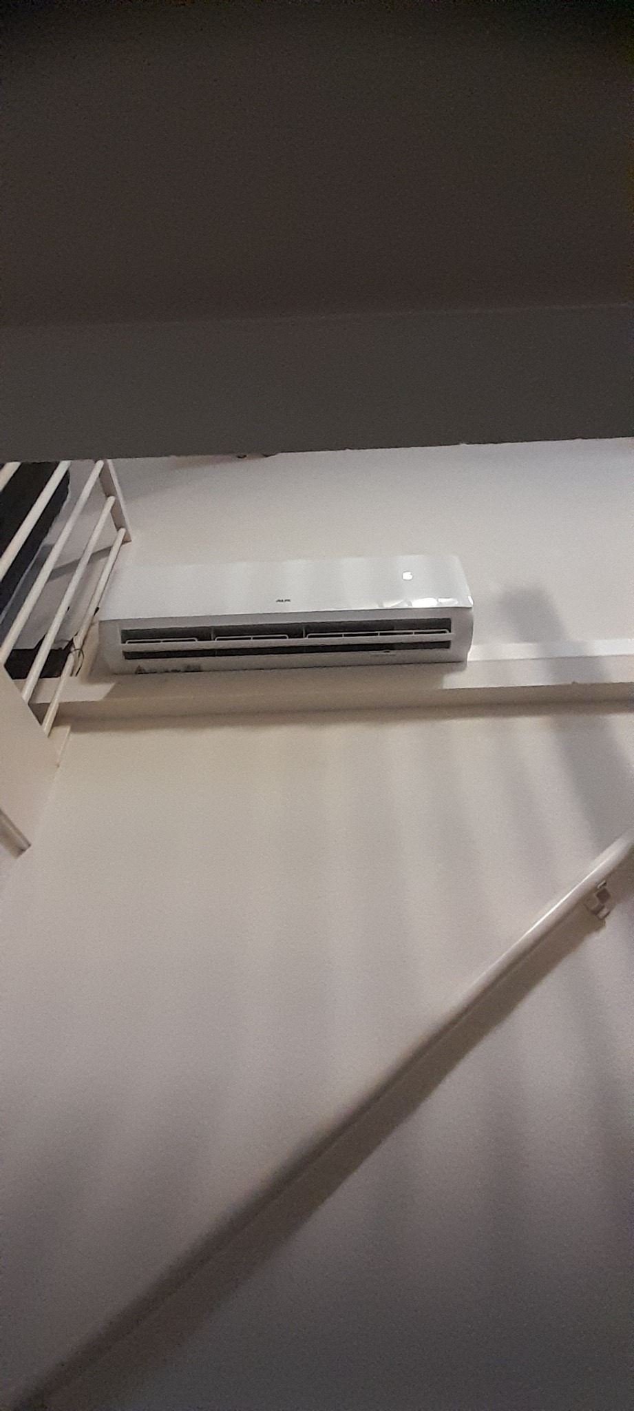 Biały klimatyzator ścienny marki AUX, zamontowany w jasnym pomieszczeniu, widok z dołu.