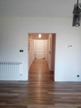 Wnętrze mieszkania po remoncie z widoczną instalacją elektryczną: grzejnik z podłączonymi przewodami, gniazdka elektryczne na ścianie, widok na korytarz z oświetleniem.