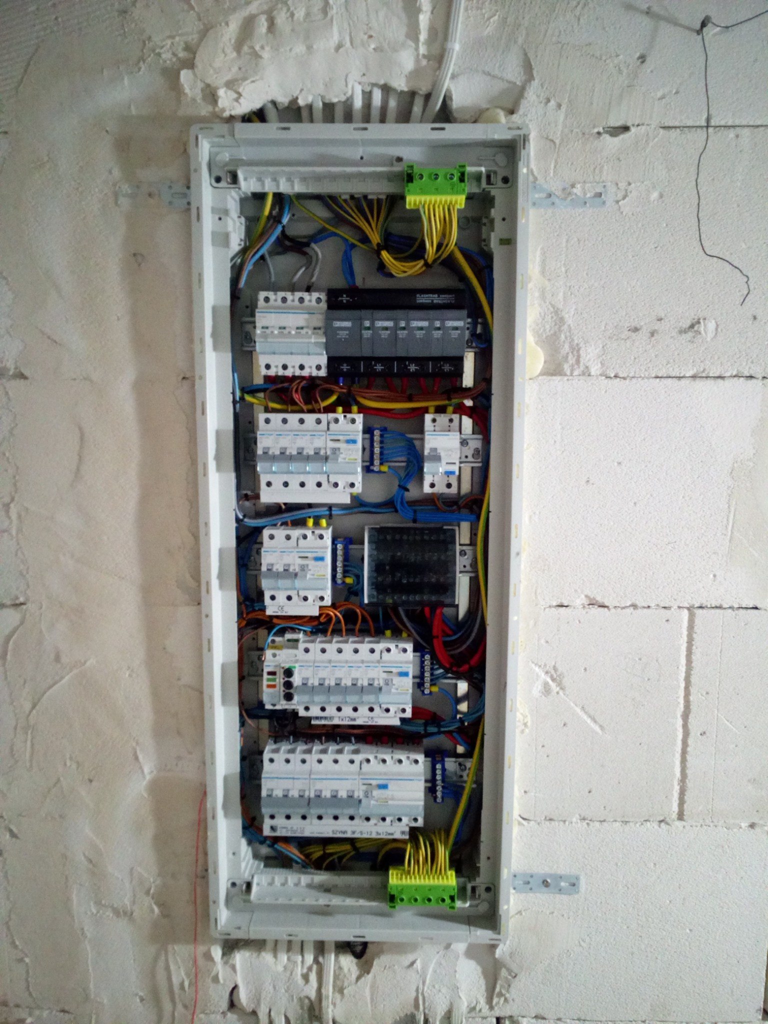 Otwarta skrzynka rozdzielcza z zainstalowanymi bezpiecznikami i okablowaniem, zamontowana na surowej ścianie z betonu komórkowego.