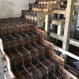 Zbrojenie schodów w szalunku z desek, widoczne pręty stalowe i drewniane podpory, surowy stan budowy.