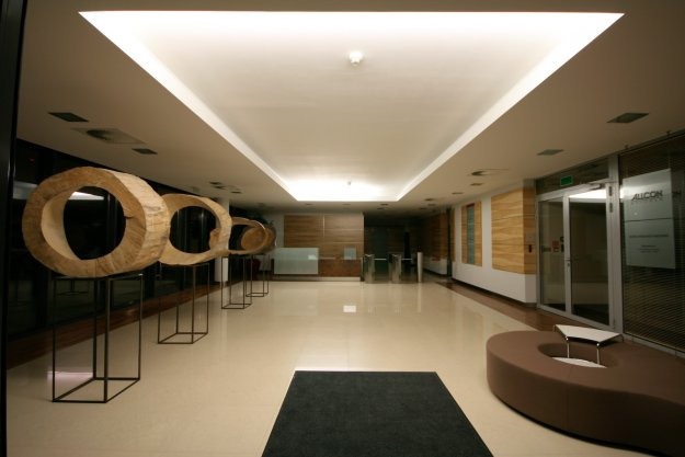 Hol w Józefowie z nowoczesnym oświetleniem sufitowym i drewnianymi rzeźbami w kształcie okręgów na metalowych podstawach.