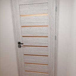 Doors-Service - Zamknięte, wewnętrzne drzwi w odcieniach szarości z poziomymi, transparentnymi paskami, czarna klamka i widoczny fragment parkietu.