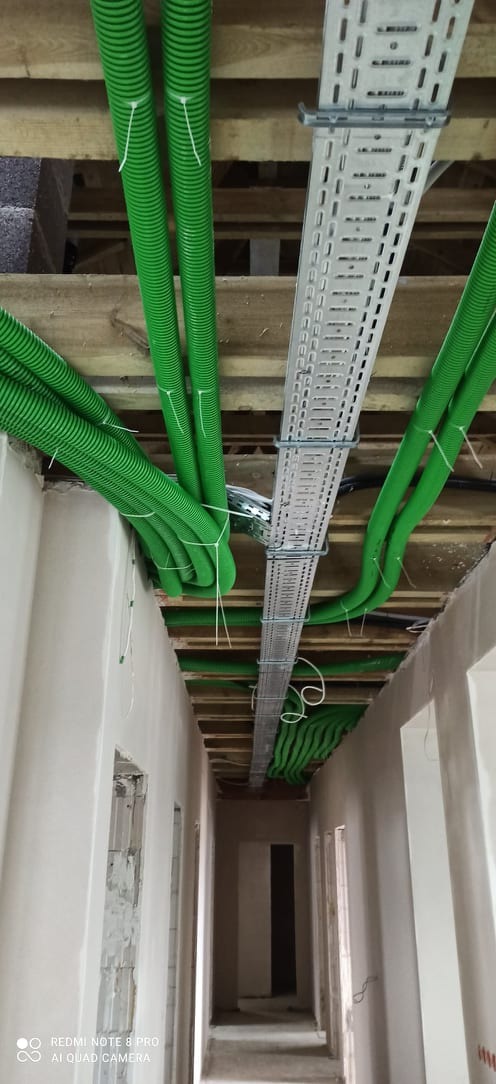 Zielone rury wentylacyjne przymocowane do sufitu w surowym stanie, widoczne koryto kablowe, instalacja w nowym budynku.