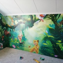 Grzegorz Idziak Anowi Usługi remontowo-budowlane - Ściana pokoju dziecięcego pokryta fototapetą z motywem Króla Lwa, widoczne narzędzia i fragment podłogi, praca w toku.