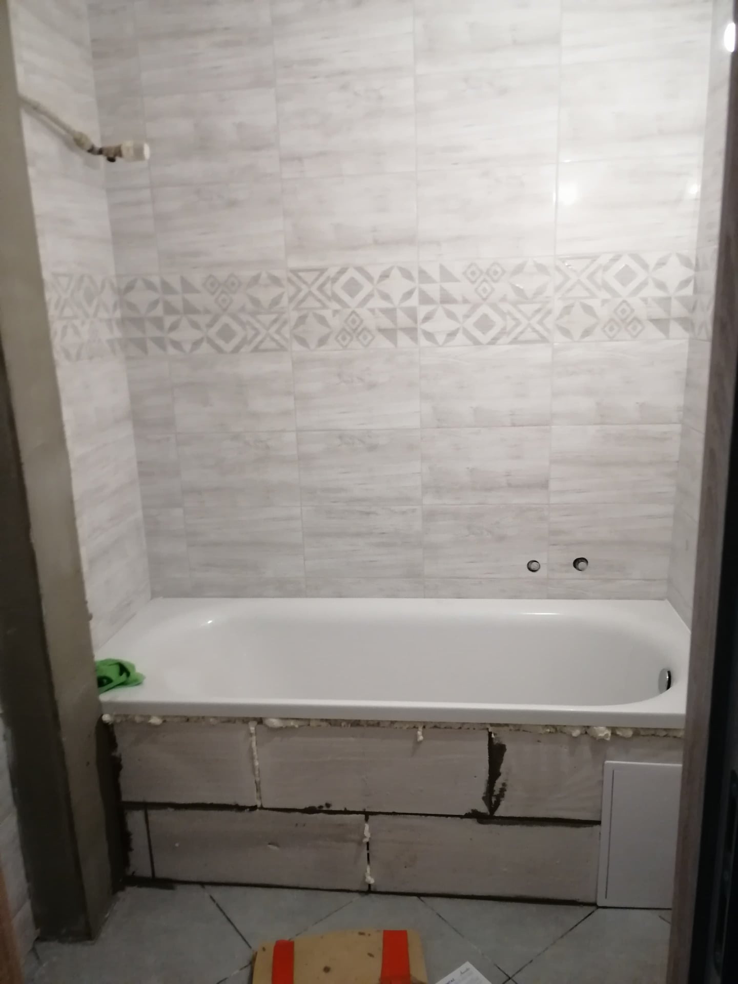 Wanna obudowana bloczkami z betonu komórkowego, białe płytki na ścianach z poziomym pasem dekoracyjnym, etap prac wykończeniowych w łazience.