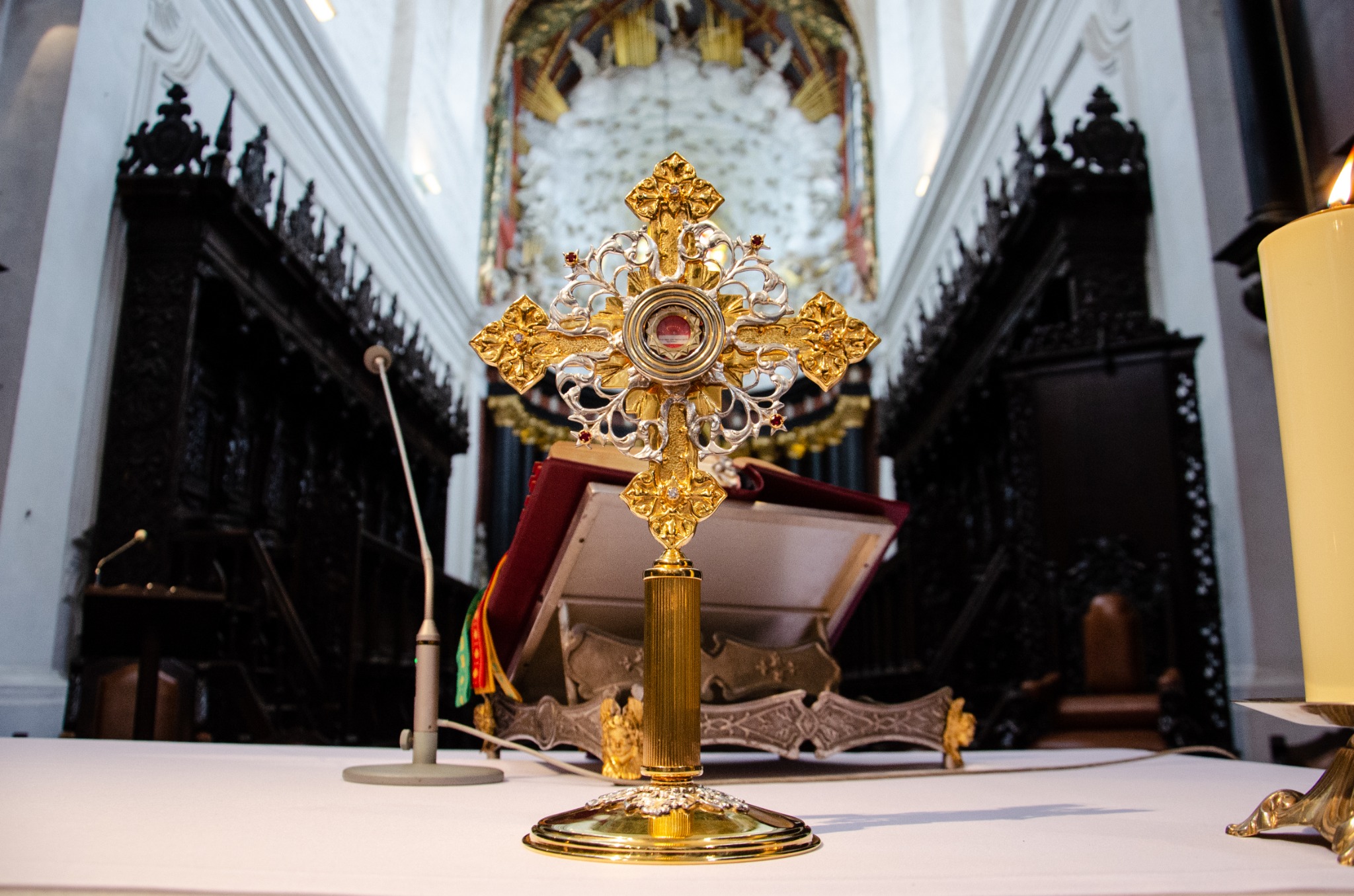 Złoty relikwiarz krzyżowy na białym ołtarzu w kościele, w tle otwarta księga liturgiczna i świeca