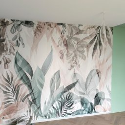 Baugrema Grzegorz Keczmerski - Ściana z fototapetą w motywy roślinne, sąsiadująca z pomalowaną na zielono ścianą, na podłodze parkiet ułożony w jodełkę.