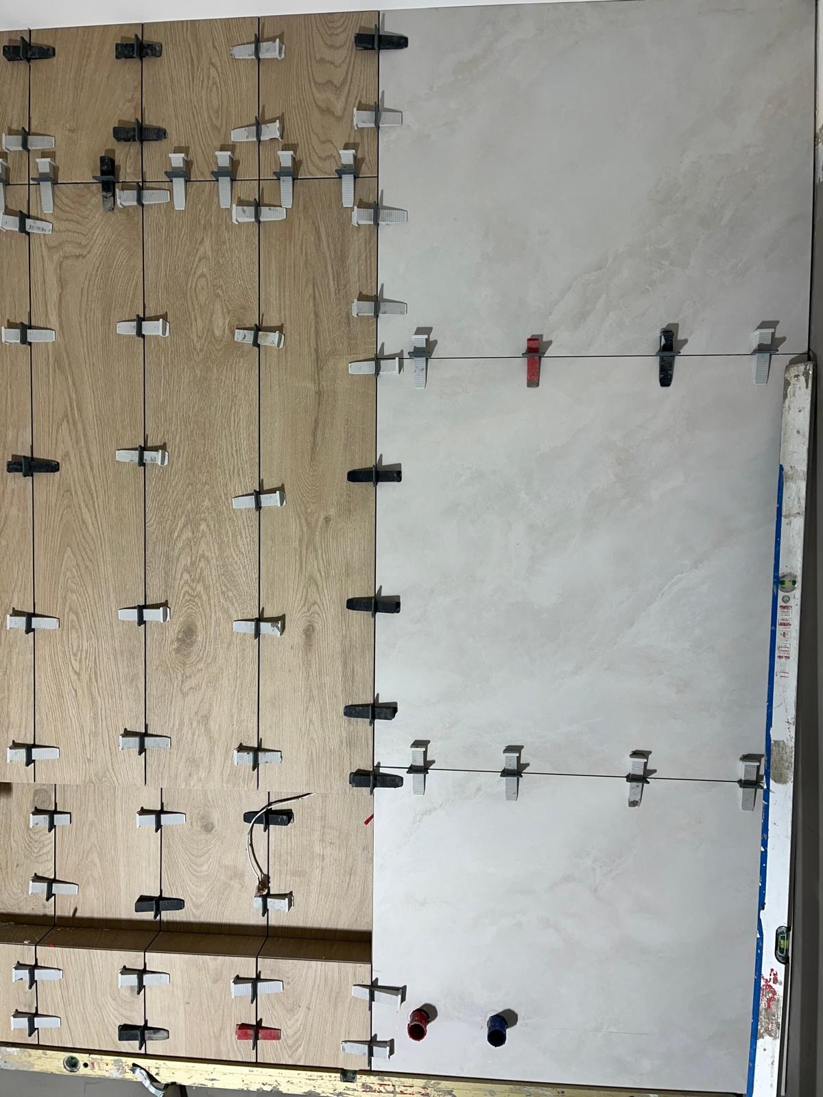 Układanie płytek imitujących drewno i jasnych płytek ceramicznych z użyciem systemu poziomowania płytek, widoczne przewody i rury.