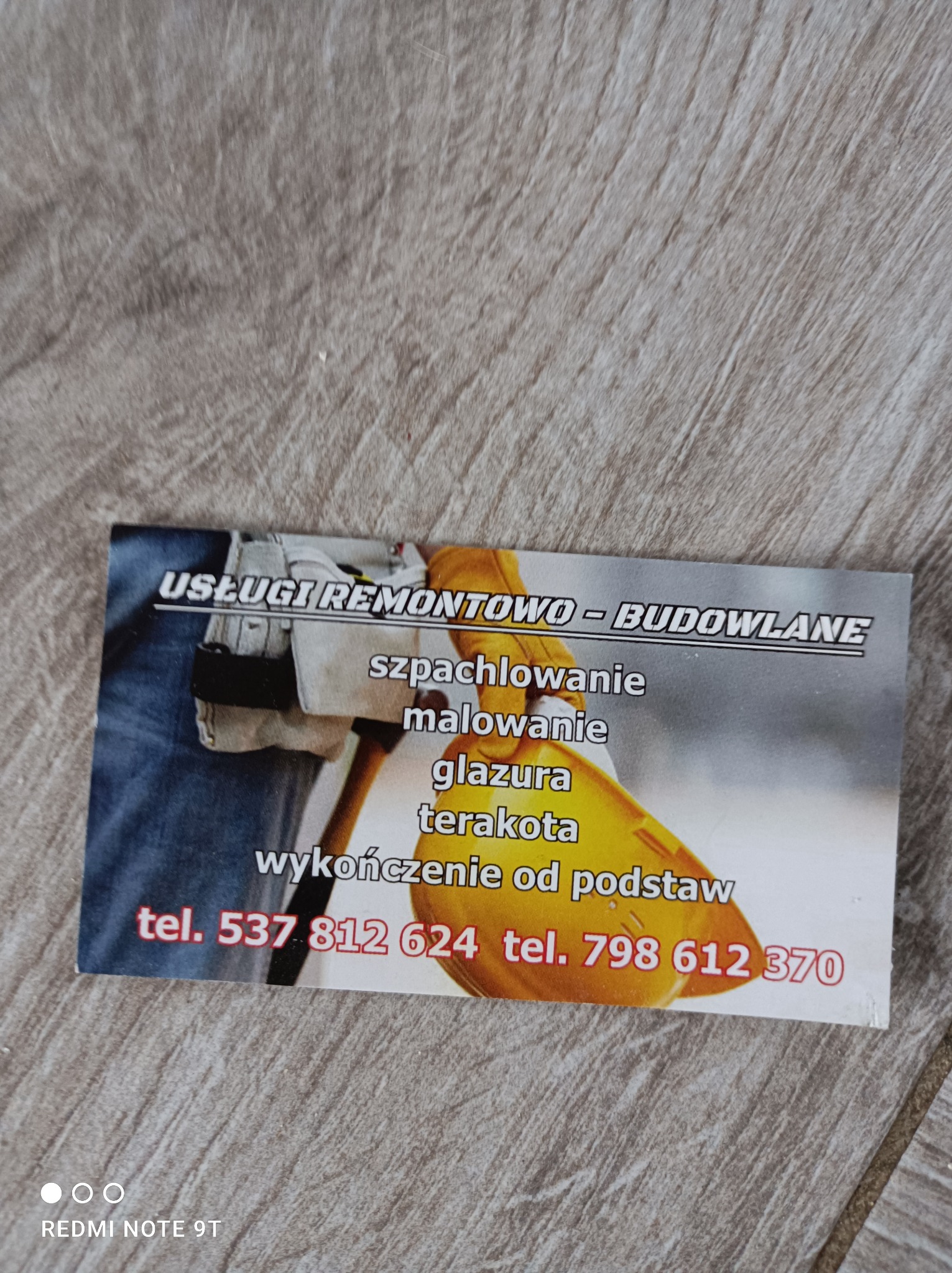 Wizytówka firmy remontowo-budowlanej z ofertą szpachlowania, malowania, glazury, terakoty i wykończeń od podstaw, leżąca na podłodze wyłożonej płytkami ceramicznymi.