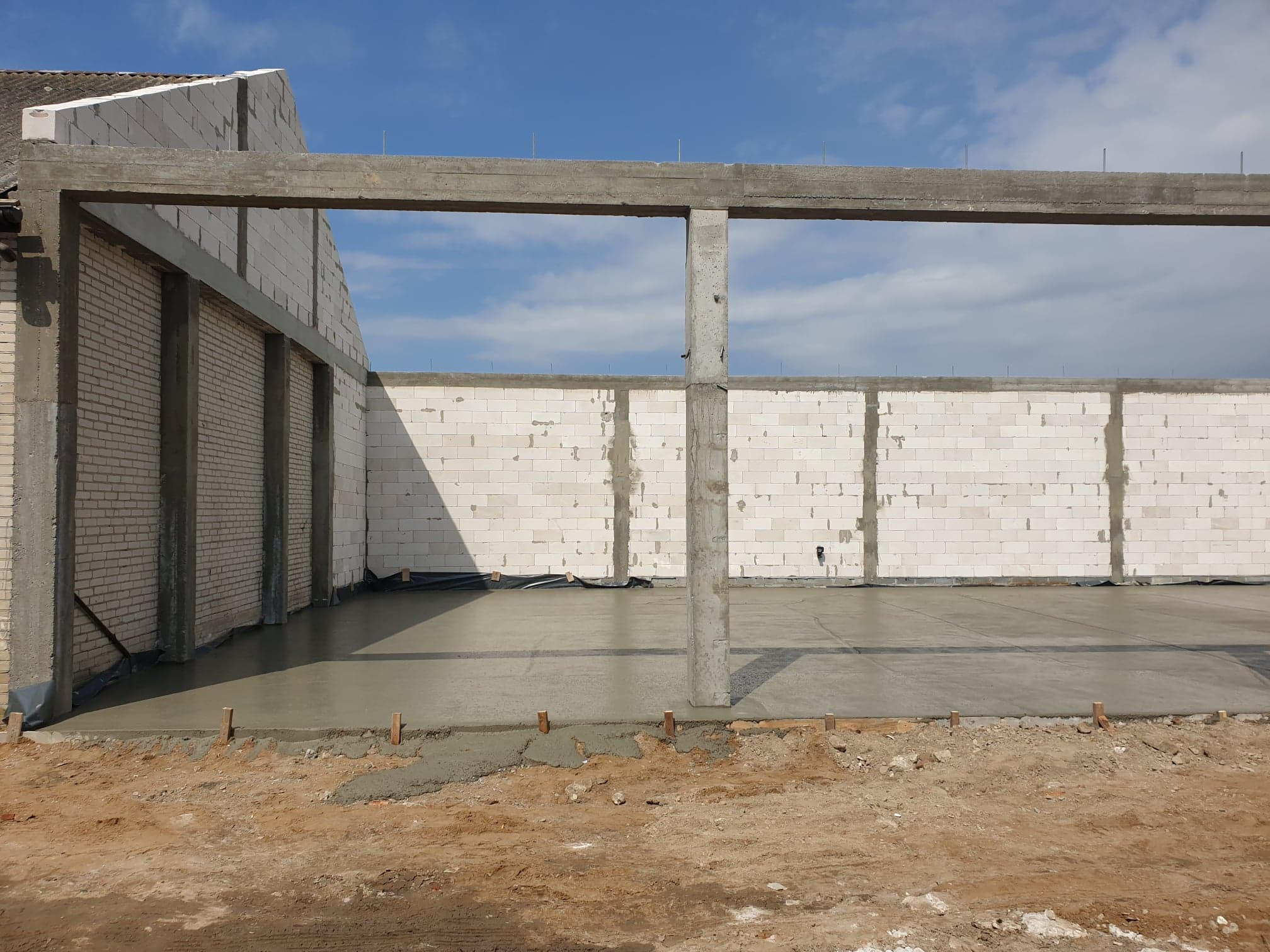 Surowy stan budynku w trakcie budowy: wylany fundament, ściany z bloczków i betonowy szkielet nośny pod przyszły dach, widok z zewnątrz.