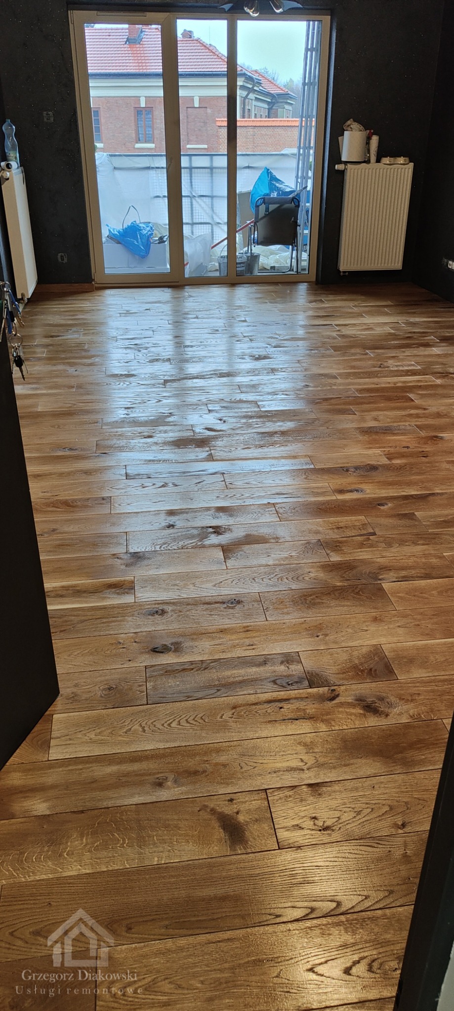 Ułożona, drewnopodobna podłoga w pokoju w Przemyślu, widok na okno balkonowe i grzejnik.