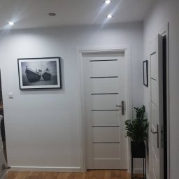 UMBT-Budziński - Białe drzwi wewnętrzne z poziomymi, czarnymi paskami w nowocześnie wykończonym korytarzu z drewnianą podłogą i minimalistycznym wystrojem.