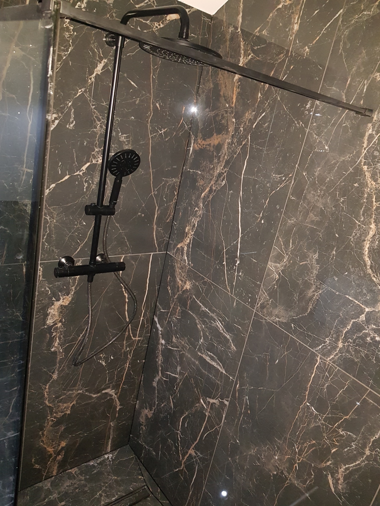 Nowoczesna kabina prysznicowa z czarną armaturą i marmurowymi płytkami w odcieniach szarości i brązu.