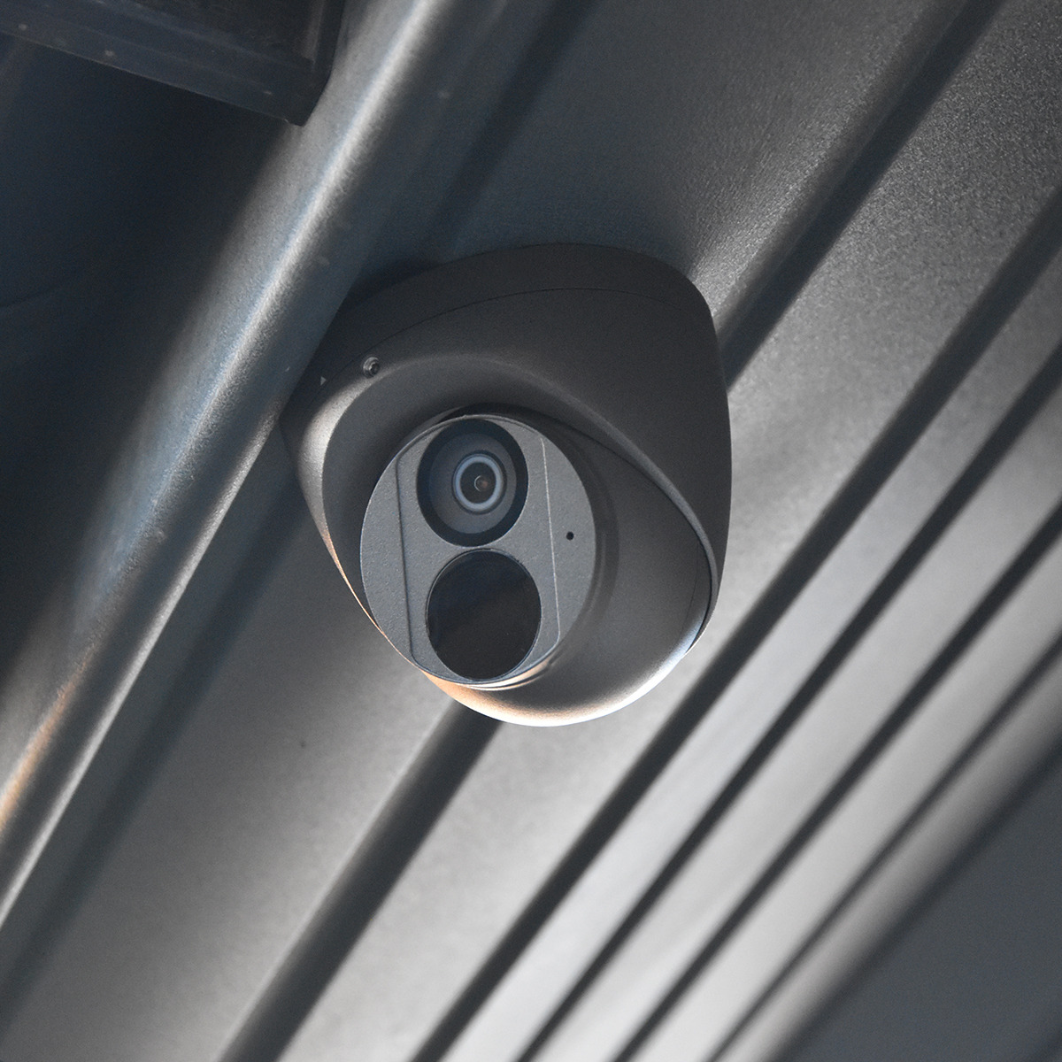 Kamera przemysłowa kopułkowa zamontowana pod metalowym dachem z widocznymi żebrami, skierowana w dół pod kątem.