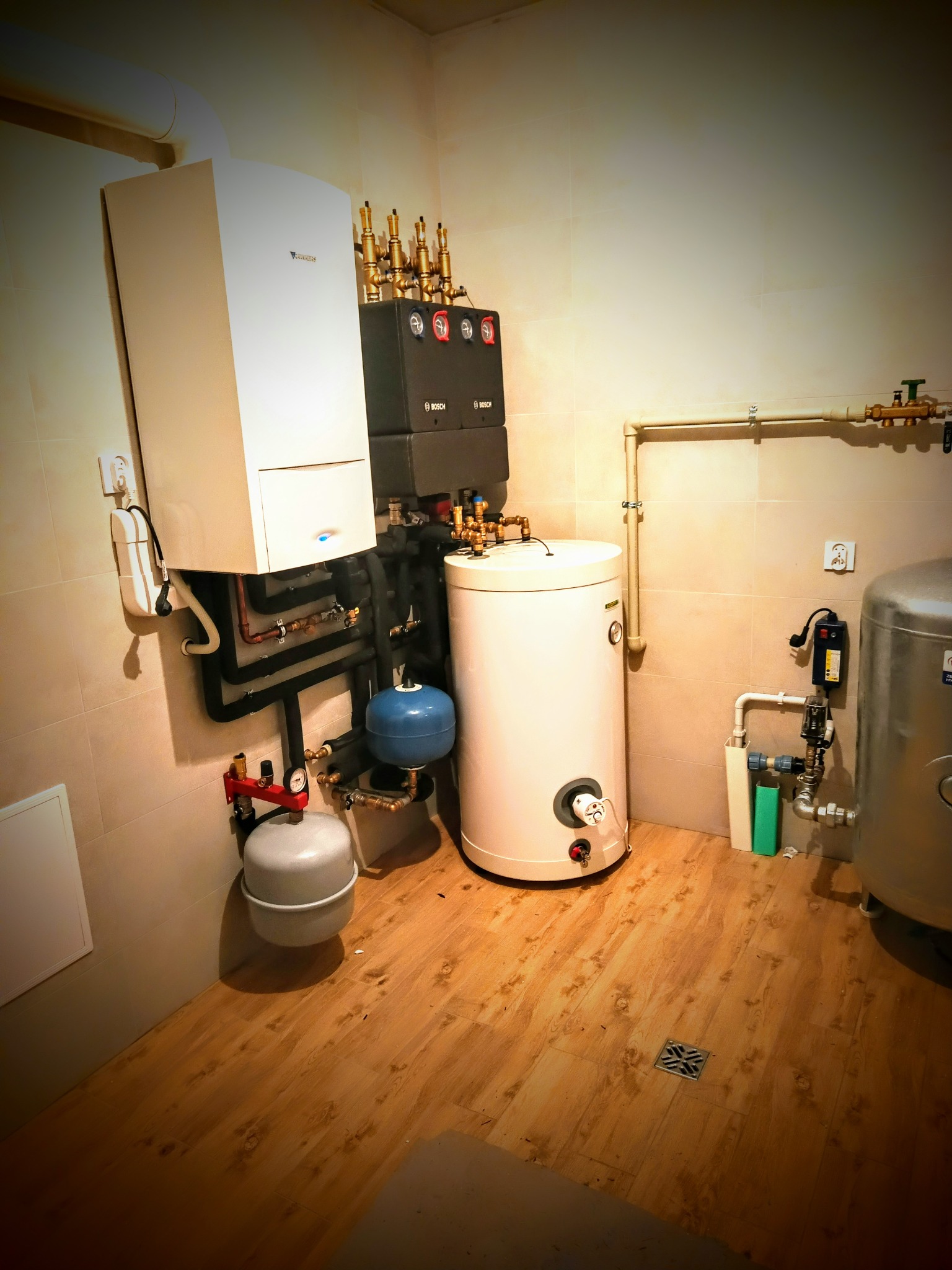 Kompleksowa kotłownia z piecem gazowym Junkers, zasobnikiem ciepłej wody, naczyniami przeponowymi i rozdzielaczem, zamontowana w pomieszczeniu z wykończonymi ścianami i podłogą.